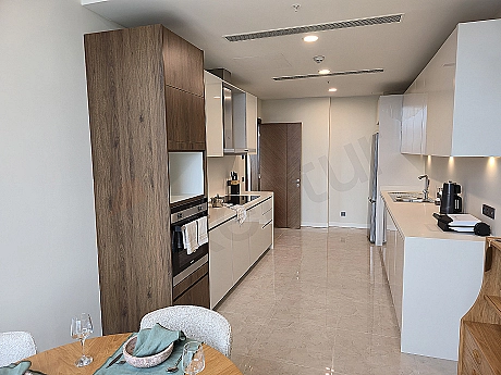 Modern tasarımlı, eşyalı lüks daire mutfağı. Açık plan mutfak, ada tezgah, ankastre beyaz eşyalar, ahşap detaylar.