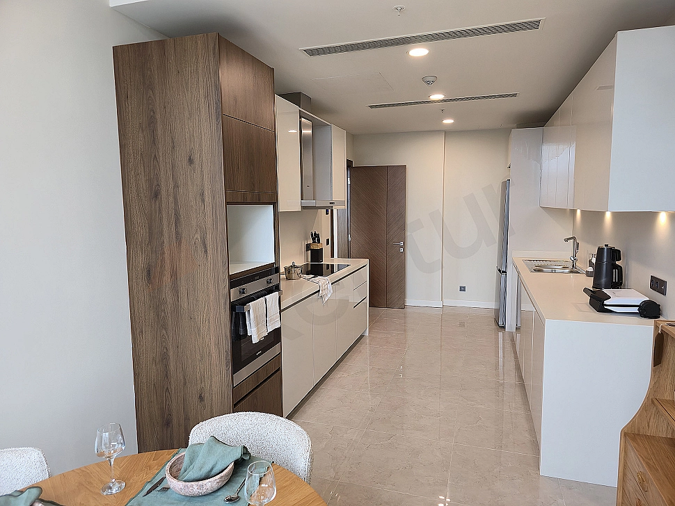 Modern tasarımlı, eşyalı lüks daire mutfağı. Açık plan mutfak, ada tezgah, ankastre beyaz eşyalar, ahşap detaylar.