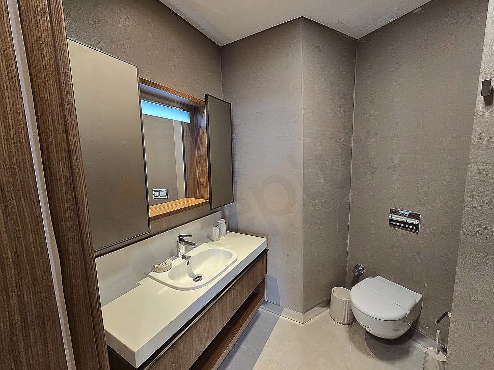 Modern tasarımlı, beyaz seramik lavabolu ve geniş aynalı lüks banyo.
