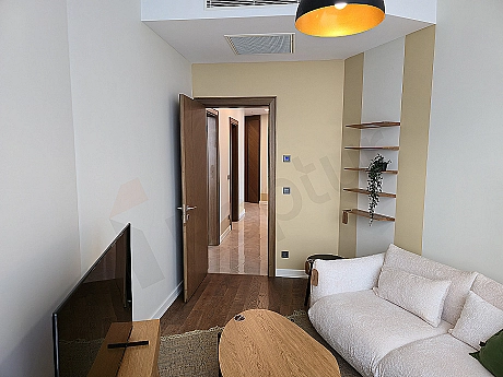 Modern çalışma odası: ahşap masa, ergonomik sandalye, kitaplık ve şehir manzaralı pencere.