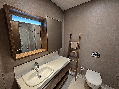 Modern tasarımlı, geniş ve aydınlık bir banyo. Beyaz seramikler, şık armatürler ve büyük bir ayna detayı.