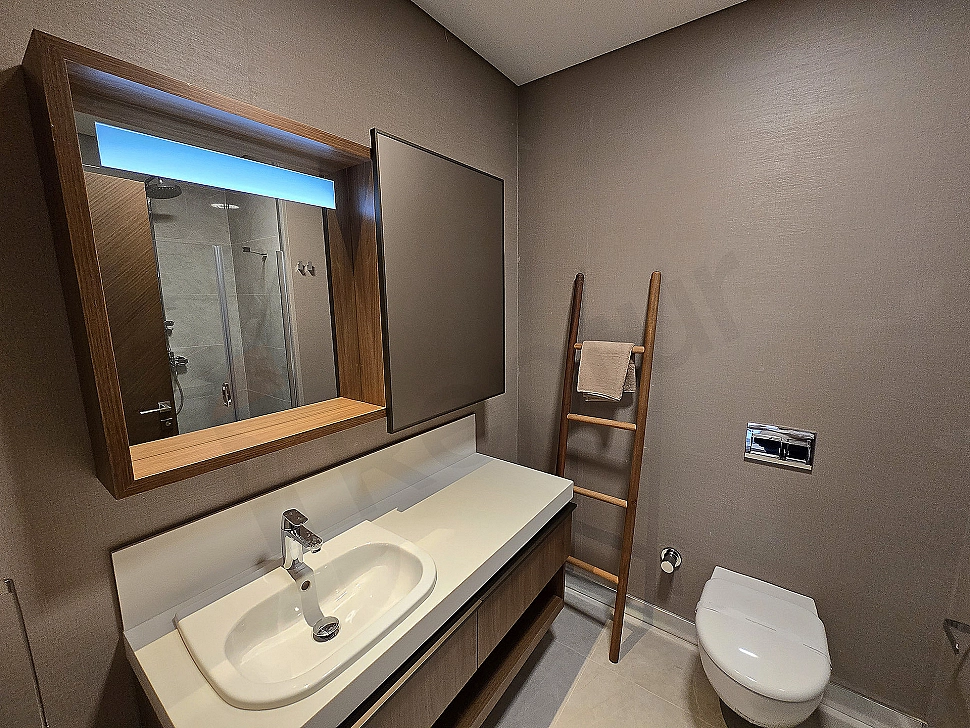 Modern tasarımlı, geniş ve aydınlık bir banyo. Beyaz seramikler, şık armatürler ve büyük bir ayna detayı.