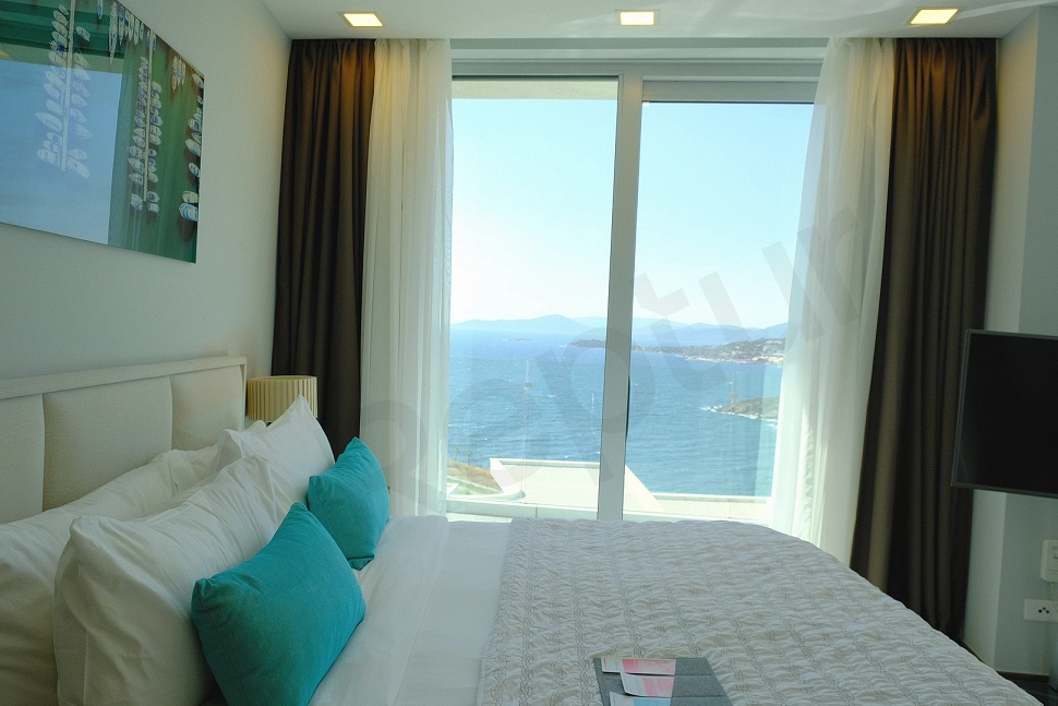 Modern ve konforlu bir yatak odası, çift kişilik yatak, iki komodin, aydınlatma armatürleri ve minimalist dekorasyona sahip.