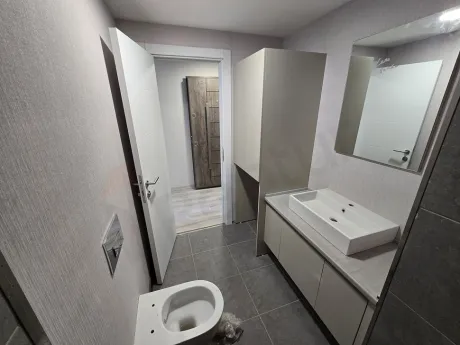 Modern seramik kaplamalı, geniş aynalı ve şık vitrifiye ürünlerine sahip banyo iç görünümü.