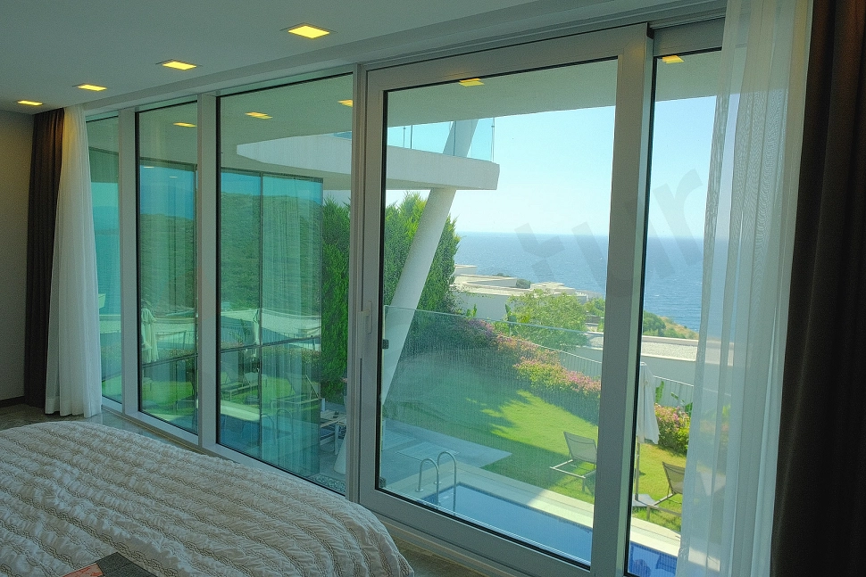 Bodrum'da denize sıfır bir villanın penceresinden görünen masmavi deniz, sahil şeridi ve ufak çizgisini kapsayan panoramik manzara.