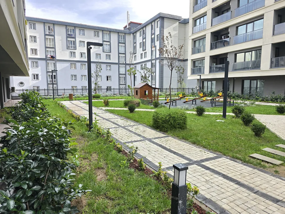 Modern bir konut sitesinin peyzajlı, yeşil bahçe alanı ve yürüyüş yolları.