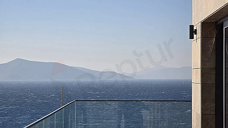 Bodrum'da bir binadan görünen masmavi deniz, kıyı şeridi ve ufuk çizgisinin panoramik manzarası.