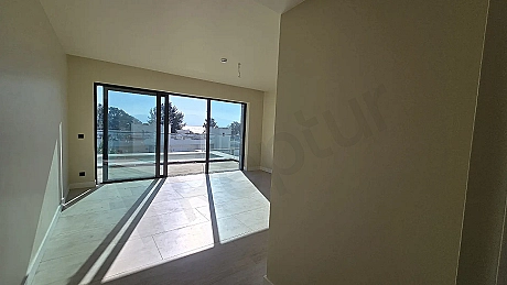 Modern bir binada yer alan geniş pencereli, aydınlık ve ferah oturma odası görünümü.