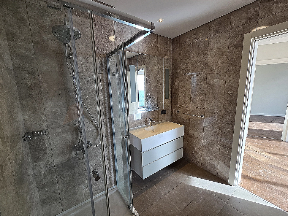 Modern tasarımlı, aydınlık ve ferah banyo iç mekanı. Beyaz seramikler, şık armatürler ve geniş duş alanı.