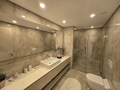 Modern tasarımlı, geniş ve aydınlık banyo. Beyaz seramikler, şık armatürler ve büyük bir pencere içeren lüks banyo.