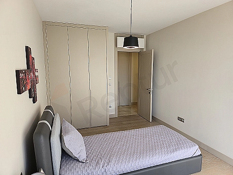 Modern tasarımlı, geniş ve aydınlık yatak odası. Ahşap detaylar, büyük pencere ve şık yatak başlığı.