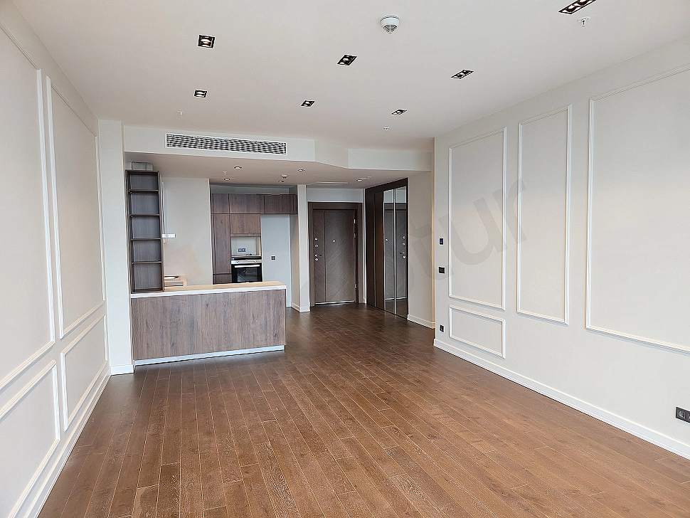 Modern oturma odası iç mekanı, geniş pencereler, ahşap parke zemin, açık renk duvarlar ve minimalist tasarım.