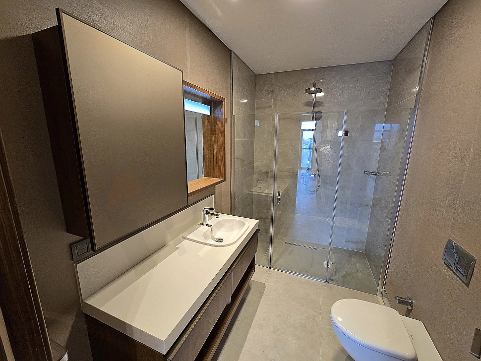 Modern tasarımlı, aydınlık ve geniş banyo. Beyaz seramikler, duşakabin ve şık lavabo.