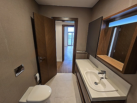 Modern tasarımlı, aydınlık ve geniş banyo. Beyaz seramikler, şık armatürler ve büyük bir ayna detayı.