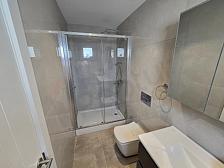Modern tasarımlı banyo iç mekanı. Beyaz fayanslar, duşakabin, lavabo ve ayna detayları.