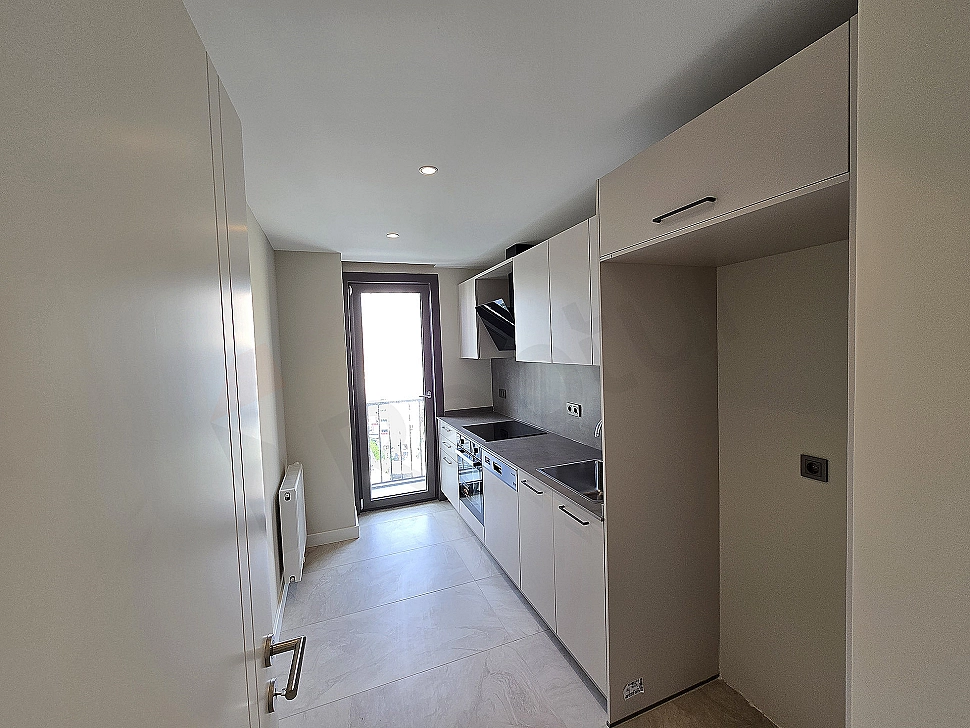 Modern beyaz mutfak dolapları, paslanmaz çelik ankastreler ve geniş pencereye sahip aydınlık mutfak.