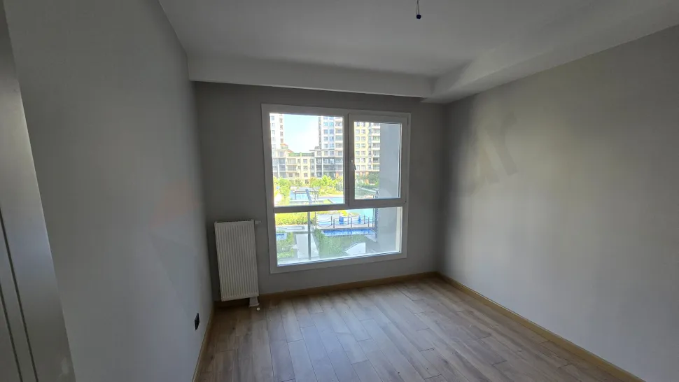 Modern mimariye sahip, geniş pencereli ve gün ışığı alan boş bir yatak odası görünümü.