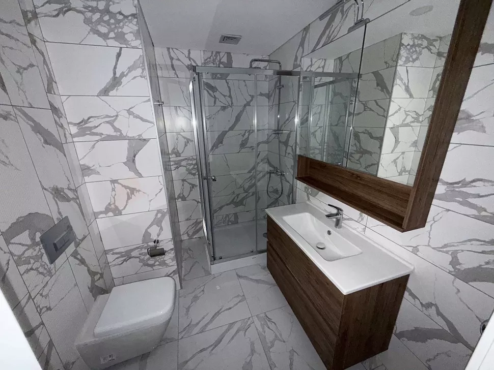 Modern tasarımlı, şık fayanslar ve vitrifiye ürünleri ile donatılmış geniş bir banyo iç mekanı.