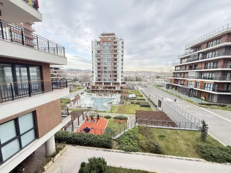 Modern bir site içerisinde peyzaj düzenlemesi yapılmış, yeşil alanları ve ağaçları olan geniş bir bahçe görünümü.