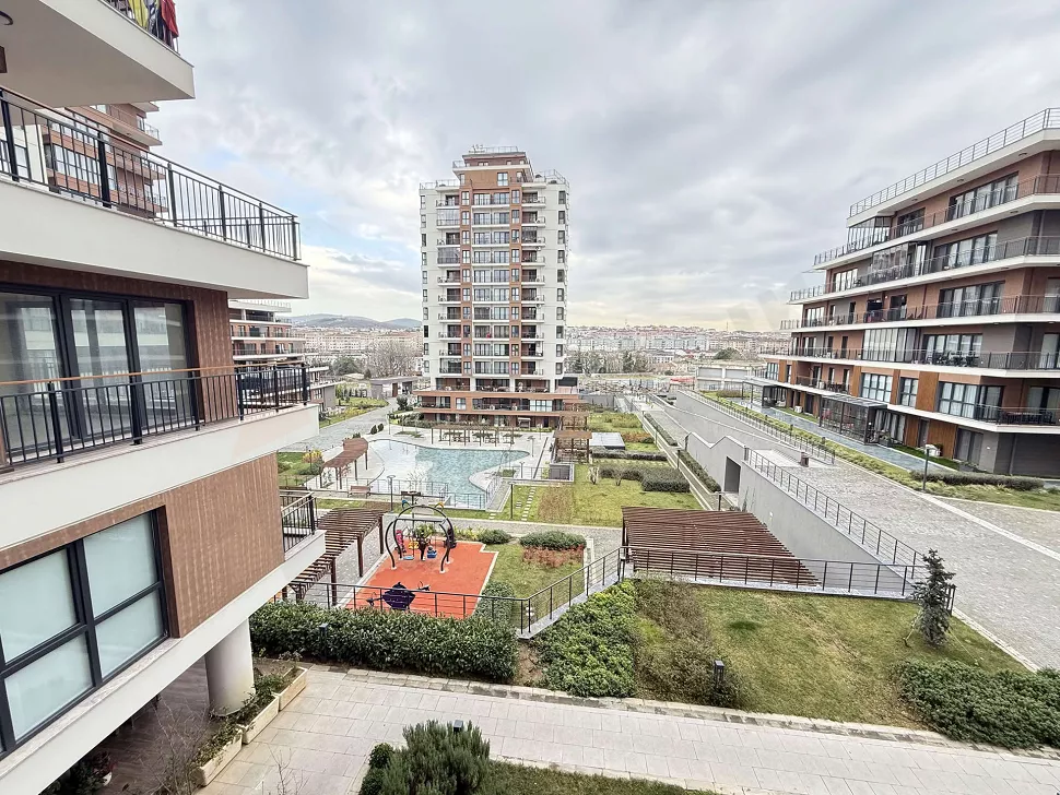 Modern bir site içerisinde peyzaj düzenlemesi yapılmış, yeşil alanları ve ağaçları olan geniş bir bahçe görünümü.