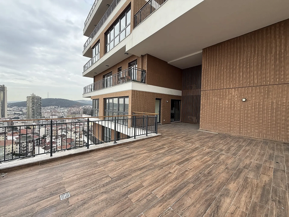 Şehir ve orman manzarasına hakim, modern bir binanın geniş ve ferah dairesine ait açık teras alanı.