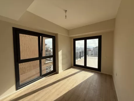 Geniş pencereli, modern zeminli ve aydınlık bir yatak odası alanı.