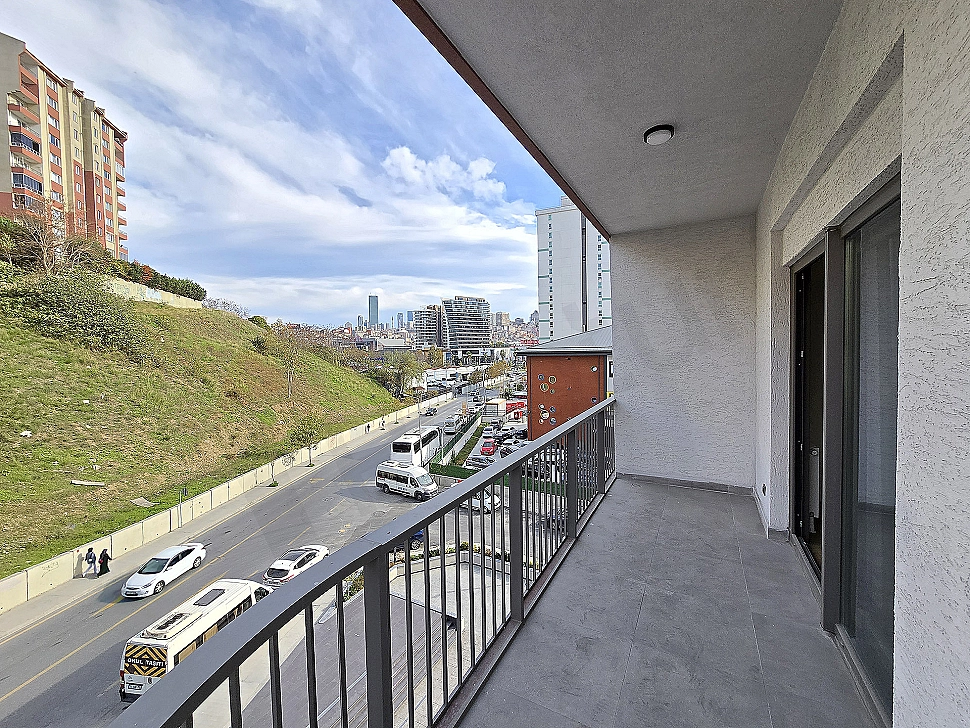 Geniş balkonlu modern daire görseli. Balkonda oturma alanı, bitkiler ve şehir manzarası.