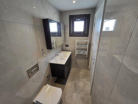 Modern tasarımlı, aydınlık ve ferah banyo iç mekanı. Beyaz seramik lavabo, geniş ayna ve şık armatürler.