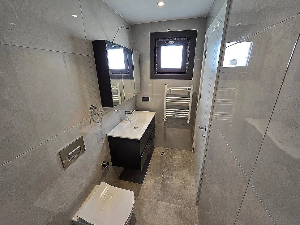 Modern tasarımlı, aydınlık ve ferah banyo iç mekanı. Beyaz seramik lavabo, geniş ayna ve şık armatürler.