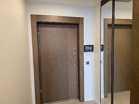 Modern tasarımlı daire giriş kapısı, ahşap detaylar, metal çerçeve ve şık aydınlatma.