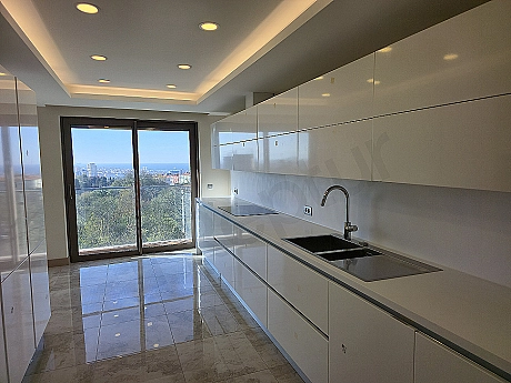 Modern beyaz mutfak dolapları, paslanmaz çelik ankastre ürünler ve geniş ada tezgahı ile aydınlık mutfak.
