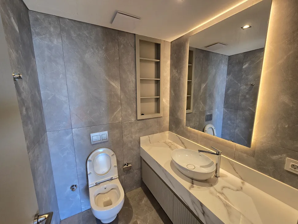 Modern tasarımlı, şık seramik ve armatürlerle donatılmış lüks bir banyo alanı.