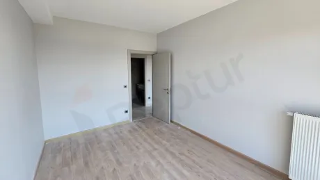Geniş pencereli, gün ışığı alan modern ve boş bir yatak odası alanı.