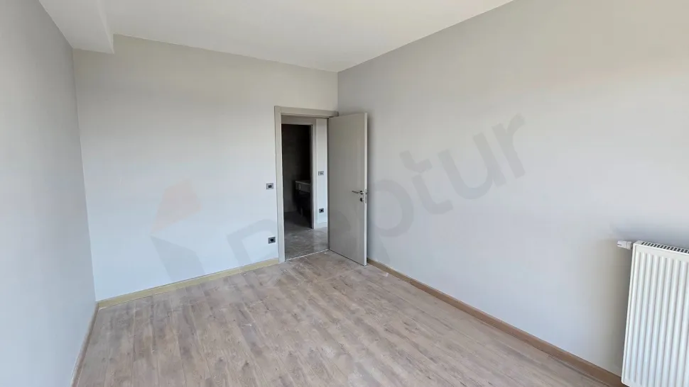 Geniş pencereli, gün ışığı alan modern ve boş bir yatak odası alanı.