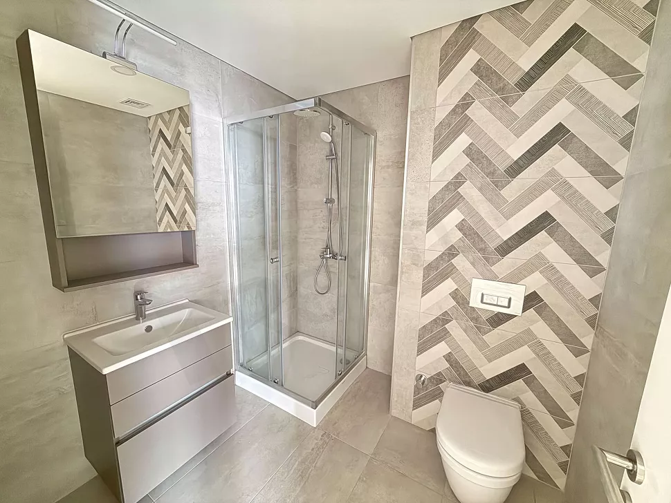 Modern tasarımlı, şık seramik döşemeli ve geniş aynalı yeni bir banyo iç mekanı.